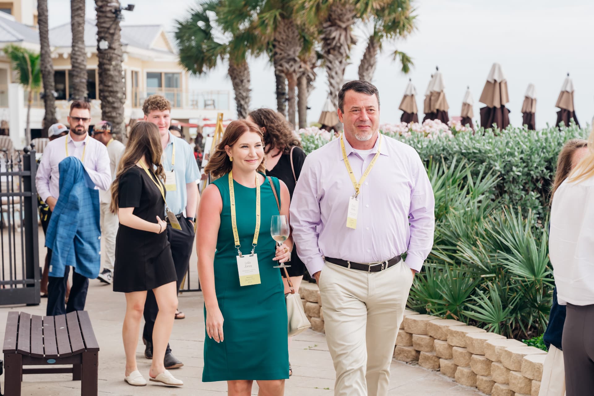 Corporate event photography of summit attendees walking a palm-lined resort path during an outdoor networking reception