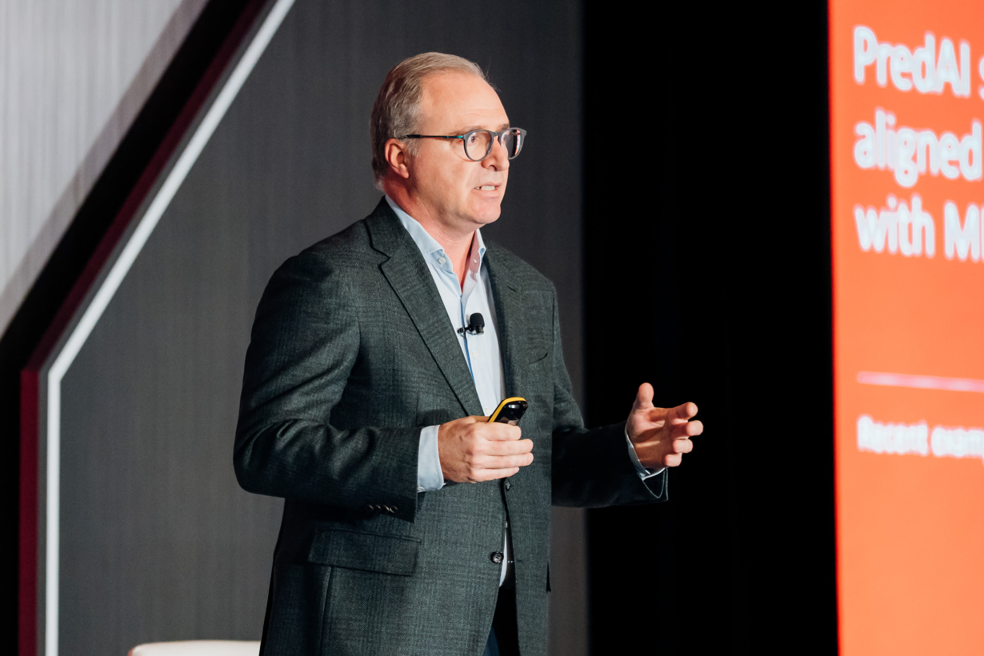Corporate event photography of an executive speaking on stage beside a large presentation screen