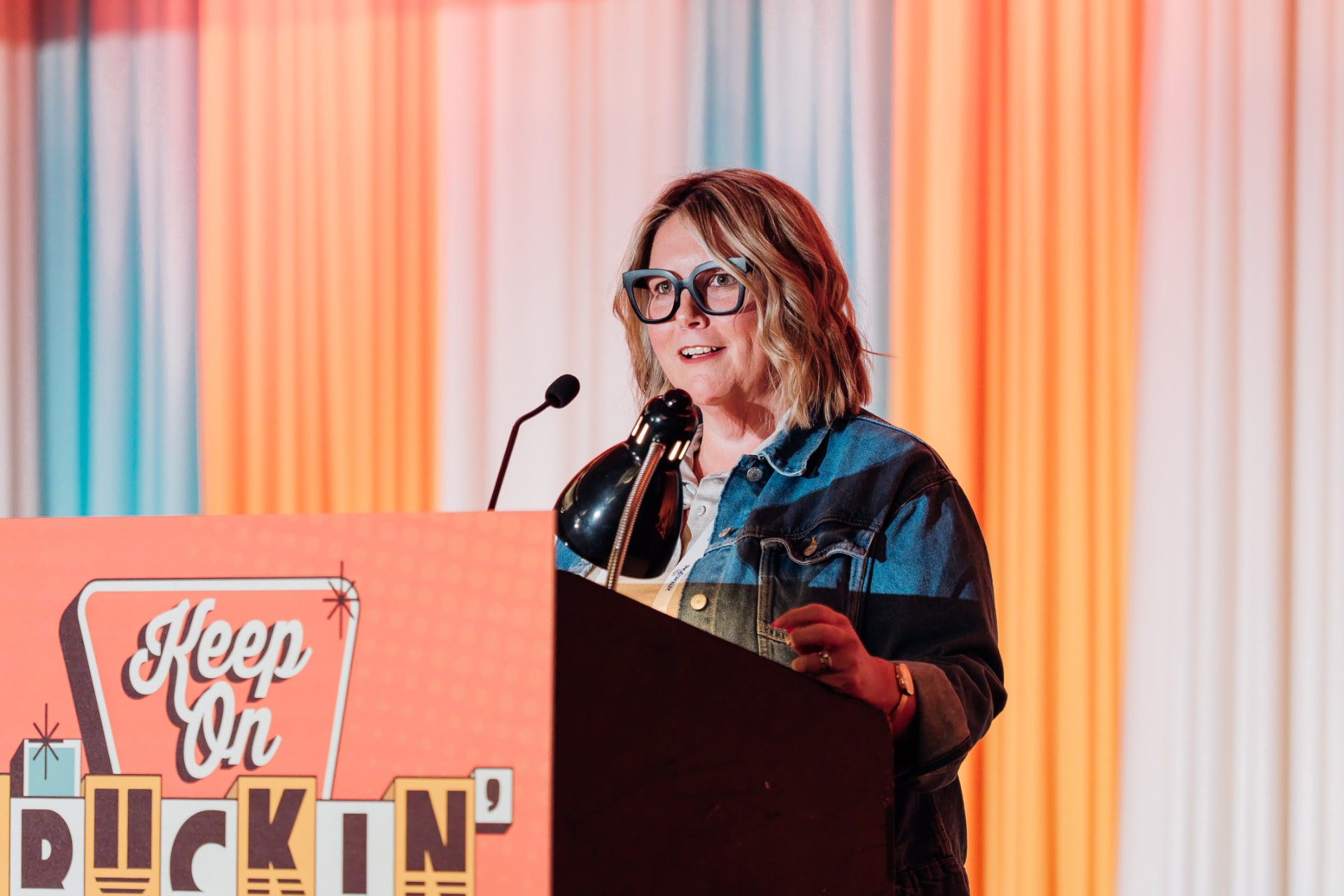Corporate event photography of a speaker presenting at a branded podium in front of a colorful draped conference backdrop