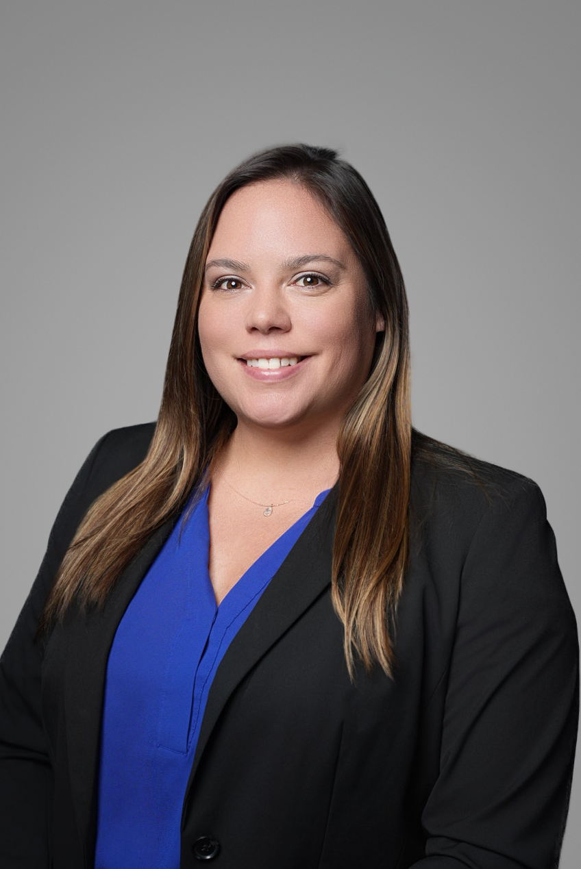 Corporate headshot of a businesswoman in a black blazer and blue blouse on a gray backdrop