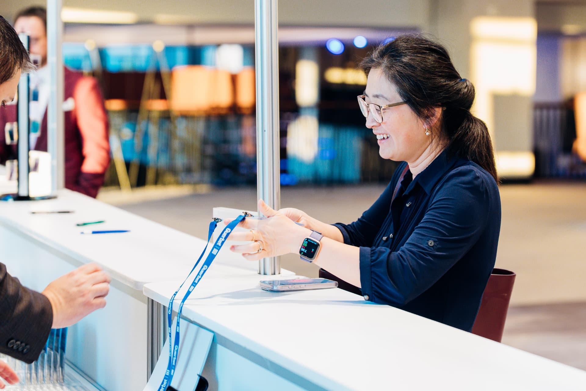 Corporate event photography of a smiling staff member handing a branded lanyard to an attendee at check-in