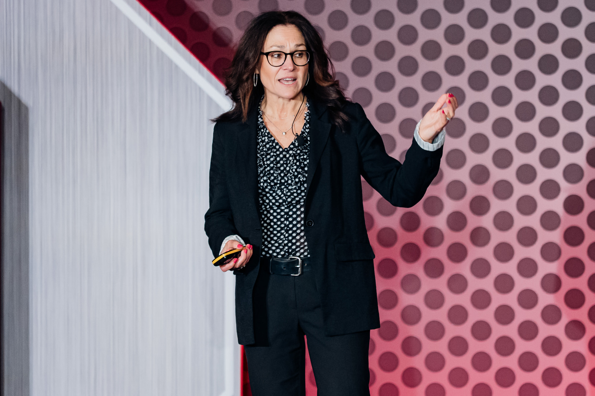 Corporate event photography of a woman presenting on stage in front of a bold patterned conference backdrop