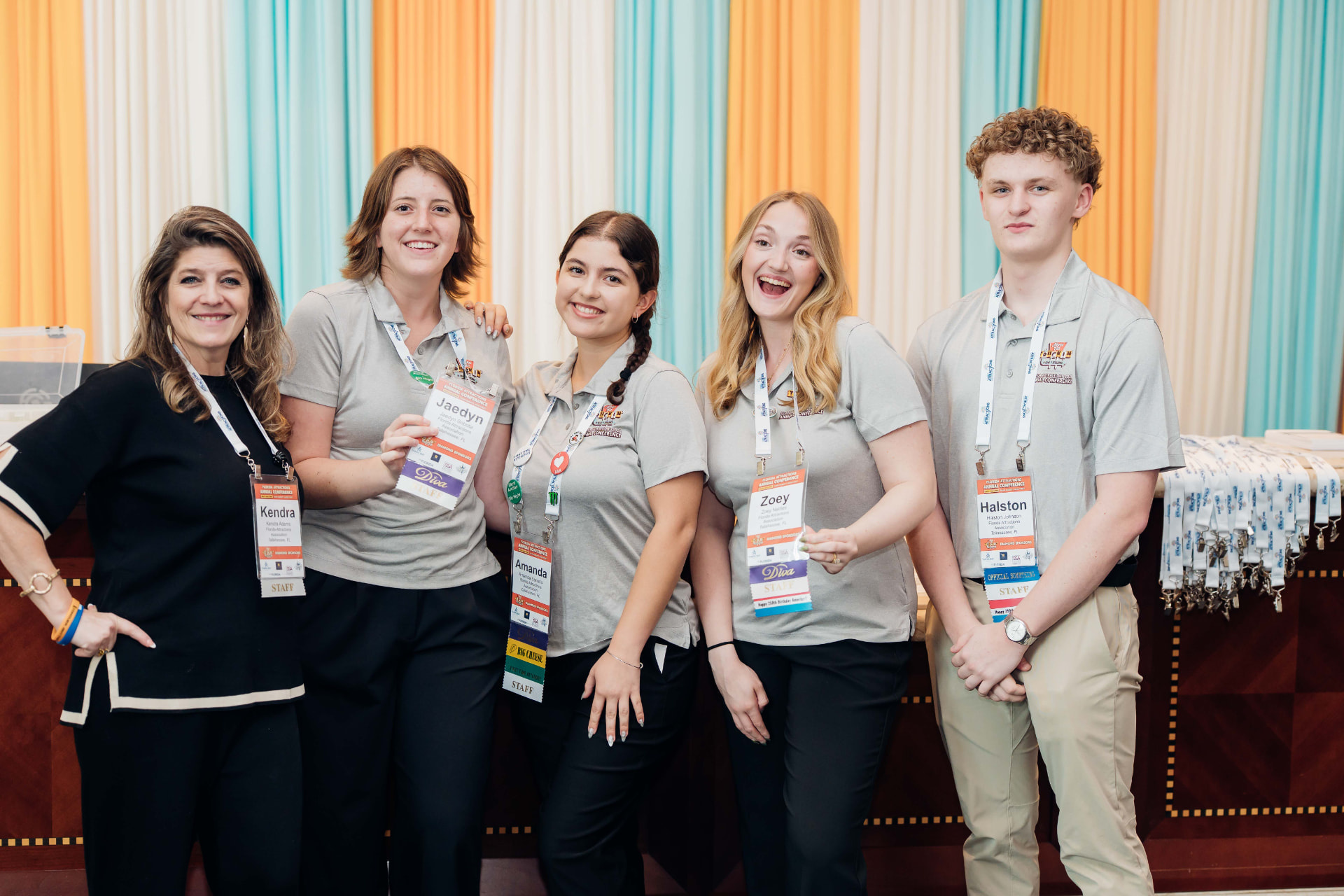Corporate event photography of a smiling conference staff team posing at the registration desk with badges and lanyards