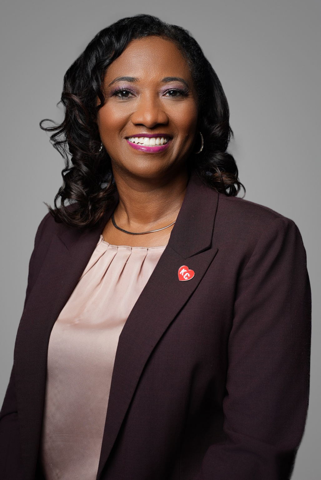 Corporate headshot of a smiling executive in a burgundy blazer on a gray studio backdrop