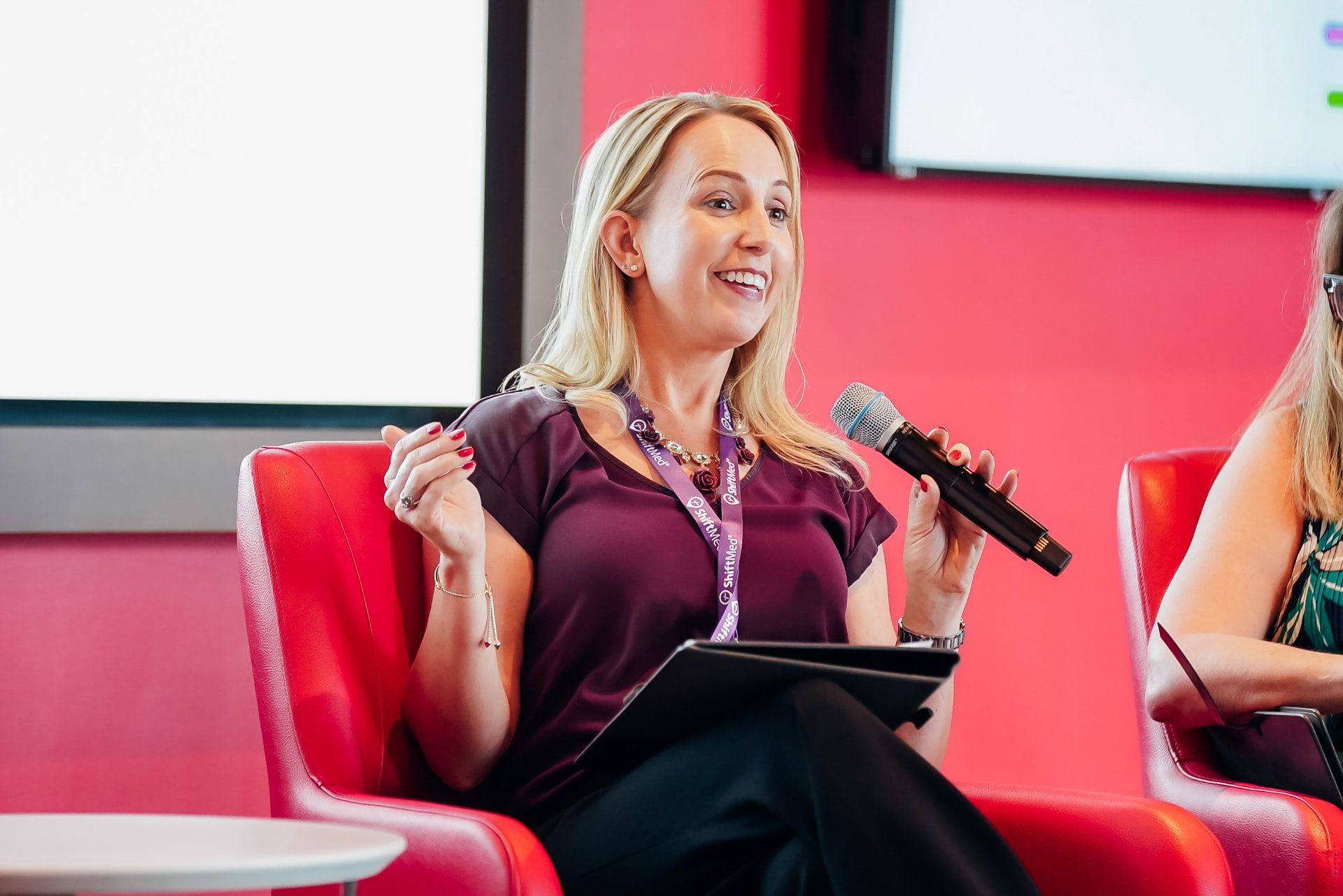 Corporate event photography of a panel speaker at a conference, seated in a red armchair with microphone — Endless Visuals Tampa Bay corporate photography