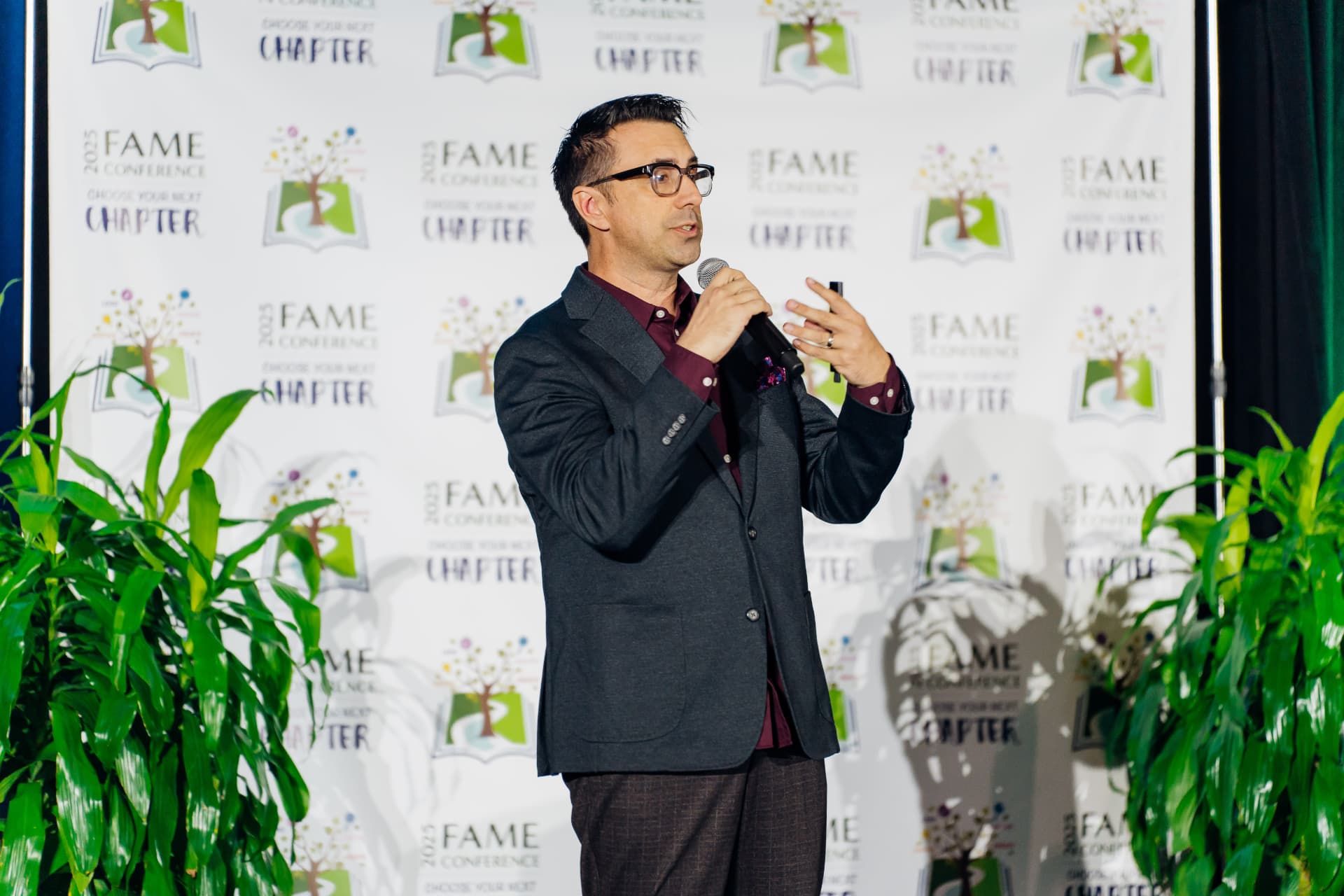 Corporate event photography of a speaker with a microphone presenting in front of a conference step-and-repeat banner