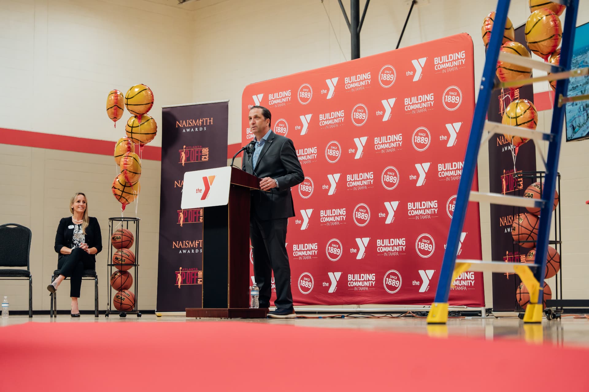 Corporate event photography of a speaker at a podium during a Naismith Awards YMCA community announcement in Tampa