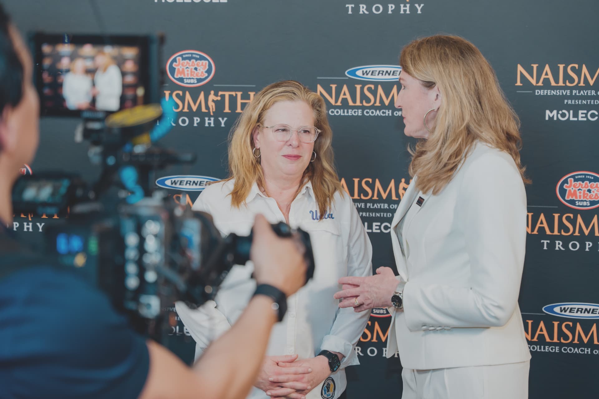 Corporate videography of a camera operator filming an on-camera executive interview at a branded step-and-repeat
