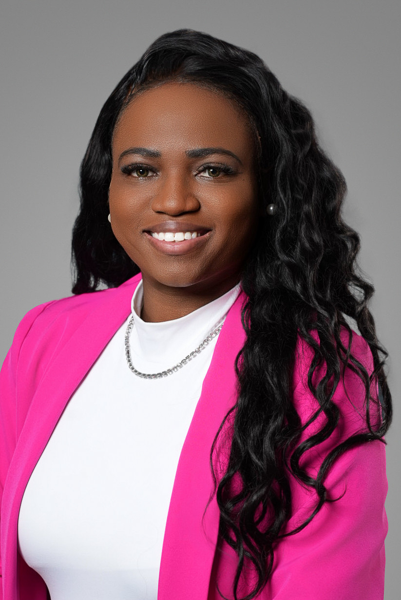 Executive headshot of a businesswoman in a pink blazer and white top on a gray studio backdrop