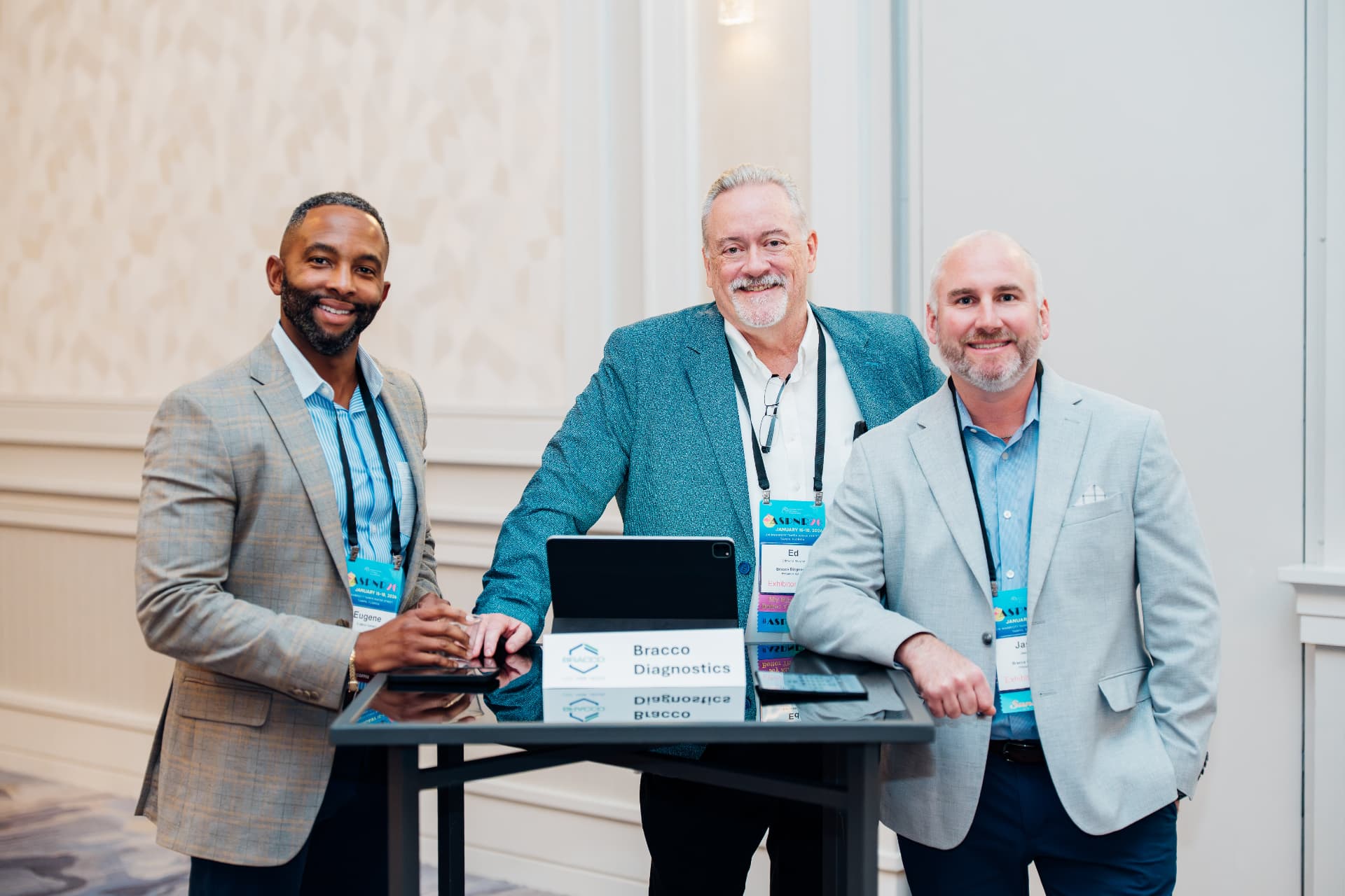 Corporate event photography of three exhibitor team members posing at a Bracco Diagnostics conference booth