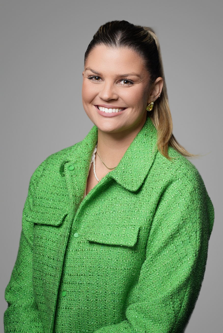 Professional headshot of a businesswoman in a bright green tweed jacket on a gray backdrop