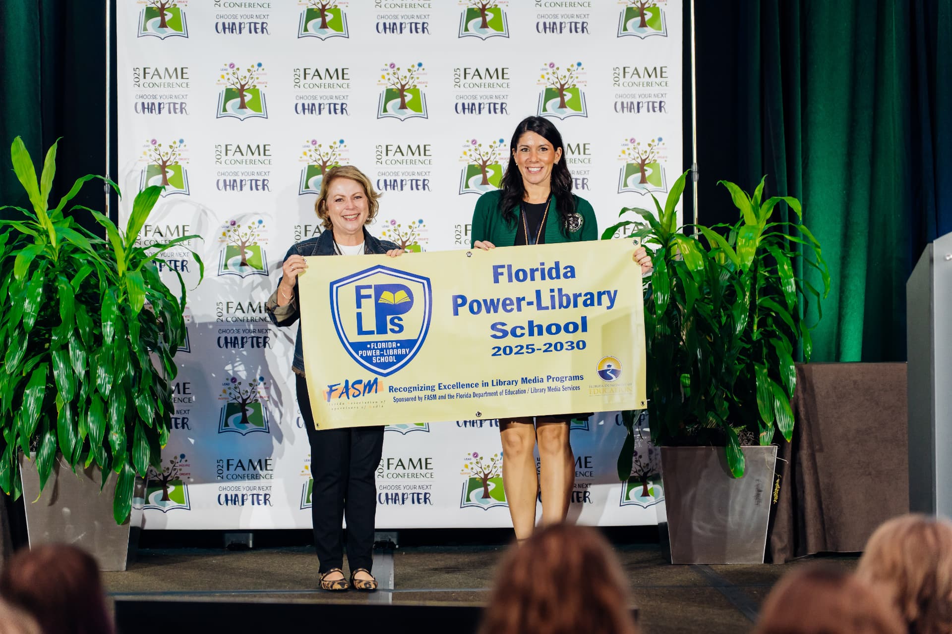 Corporate event photography of two award recipients holding a recognition banner on stage