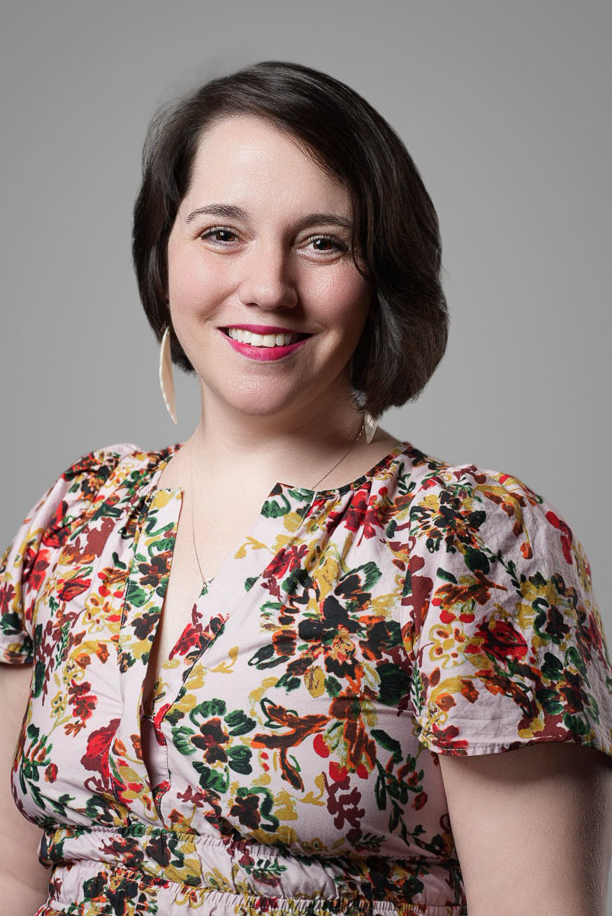 Corporate headshot of a smiling professional in a floral print blouse on a gray backdrop