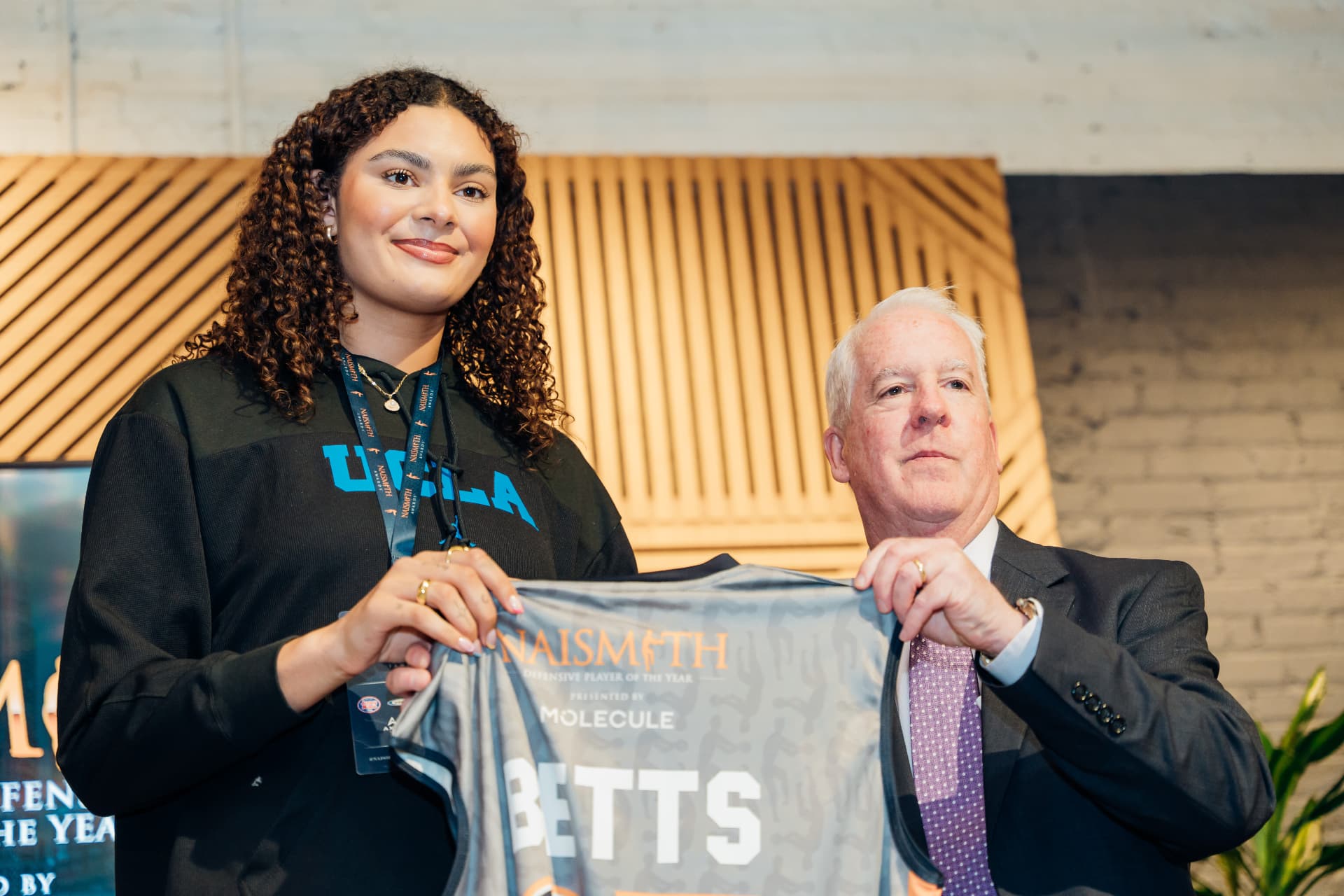 Corporate event photography of a Naismith Defensive Player of the Year jersey presentation to a UCLA athlete
