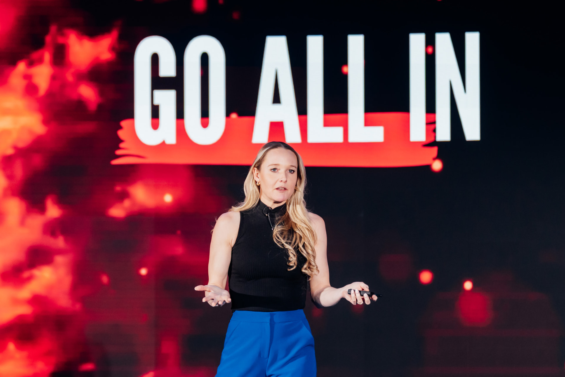 Corporate photography of a speaker on a large stage in front of a bold red LED backdrop