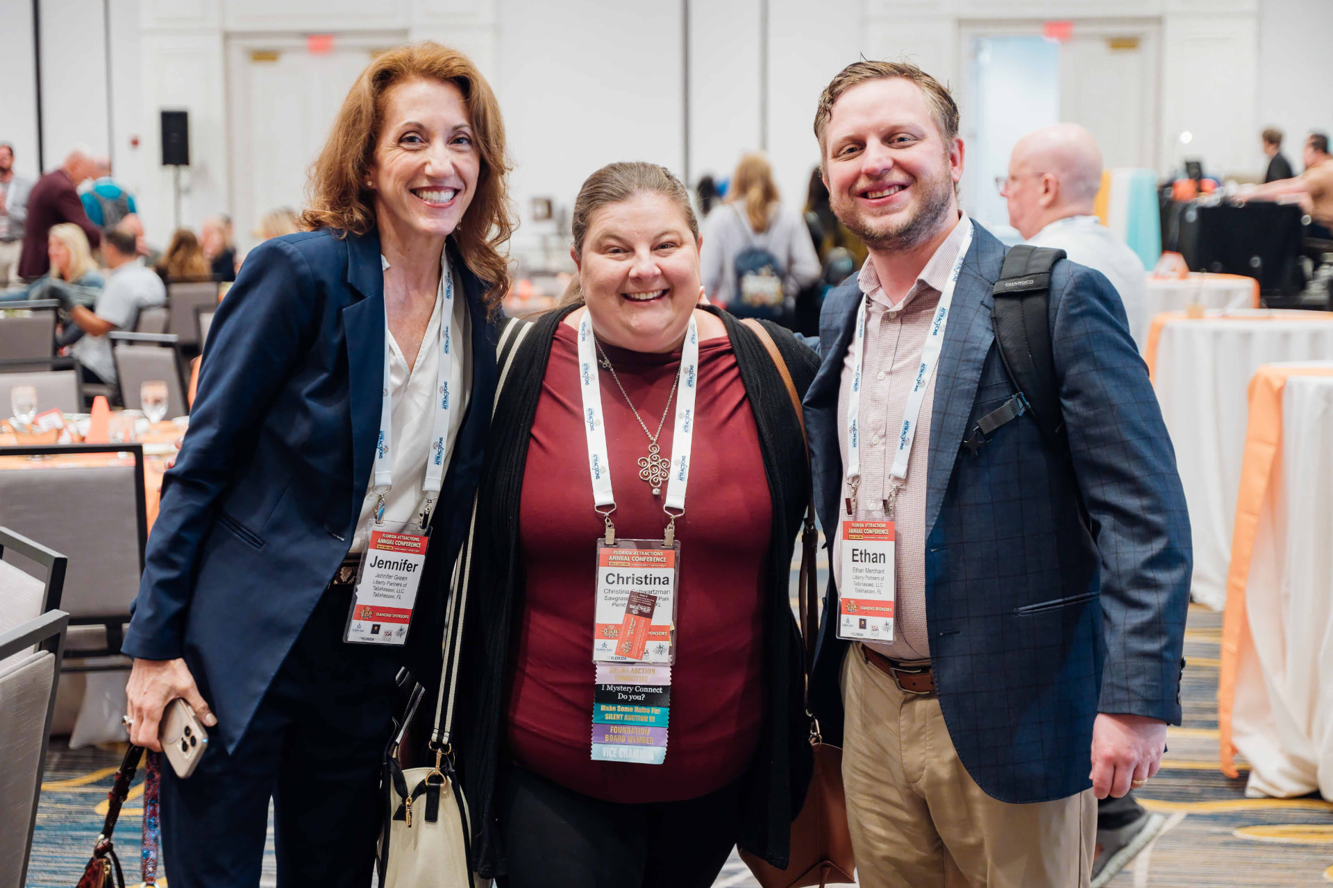 Corporate event photography of three attendees smiling together during a conference luncheon