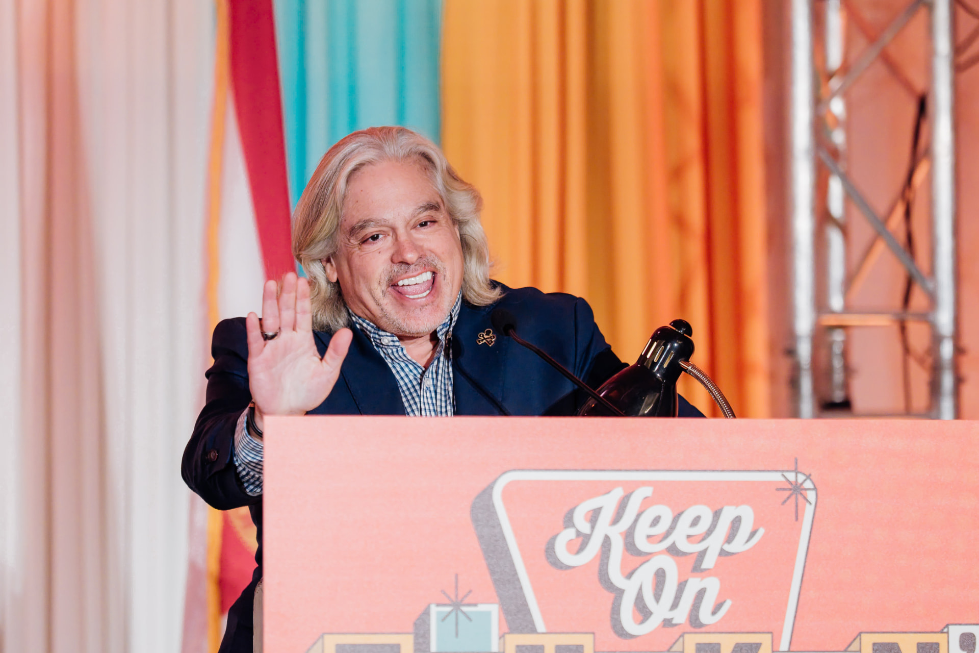 Speaker presenting at a Tampa corporate conference with a waving gesture at a colorful podium