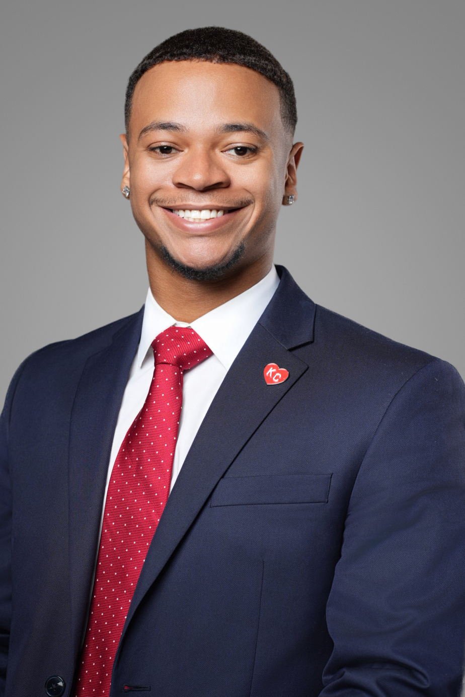 Corporate headshot of a smiling businessman in a navy suit and red tie on a gray studio backdrop