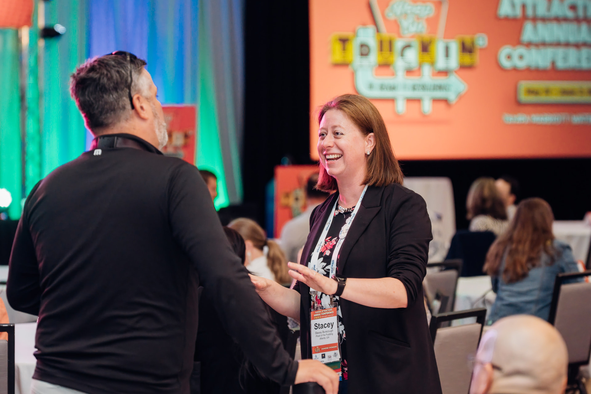 Corporate event photography of attendees greeting each other in front of a conference main stage