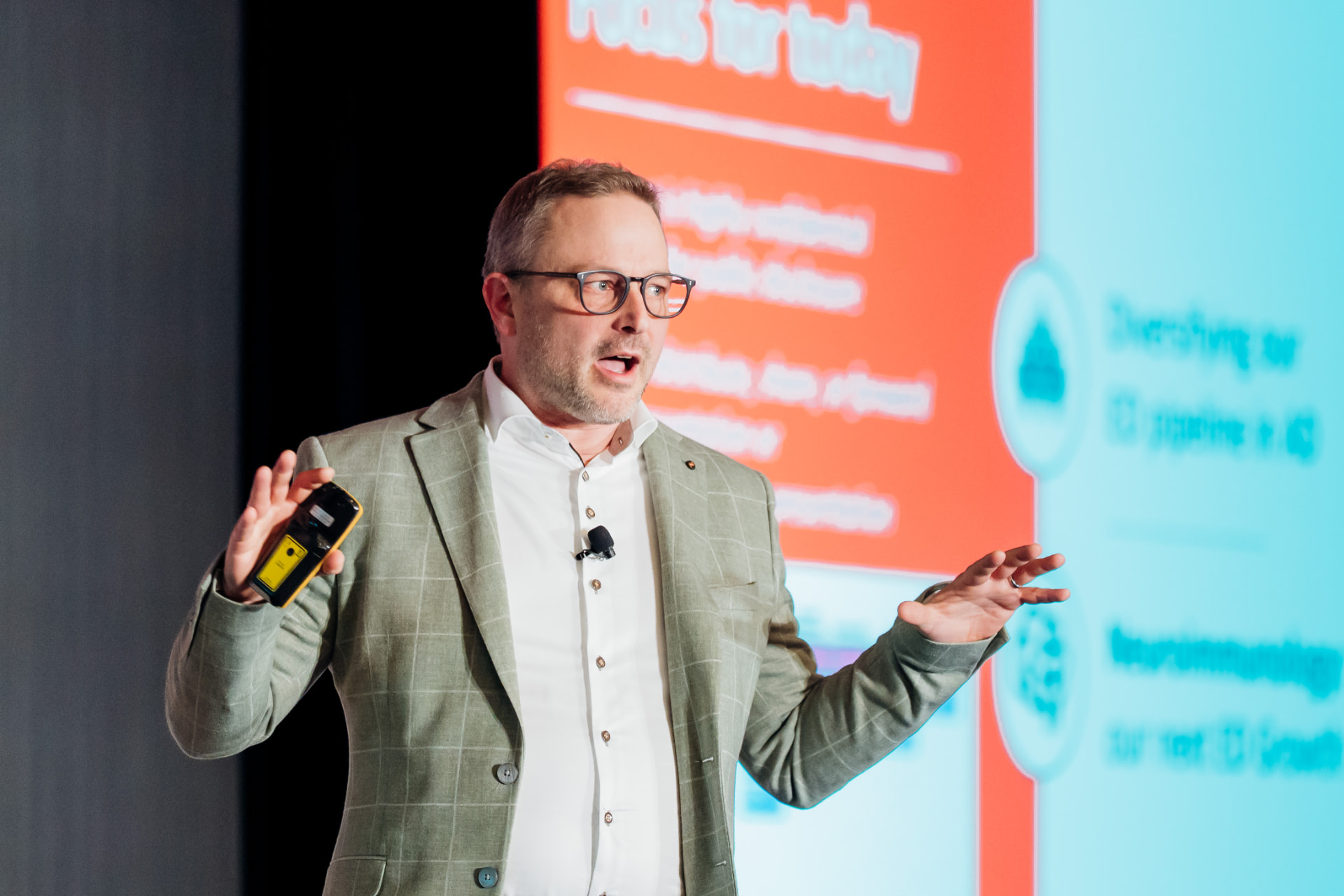 Corporate photography of a keynote speaker presenting with bold conference graphics behind him
