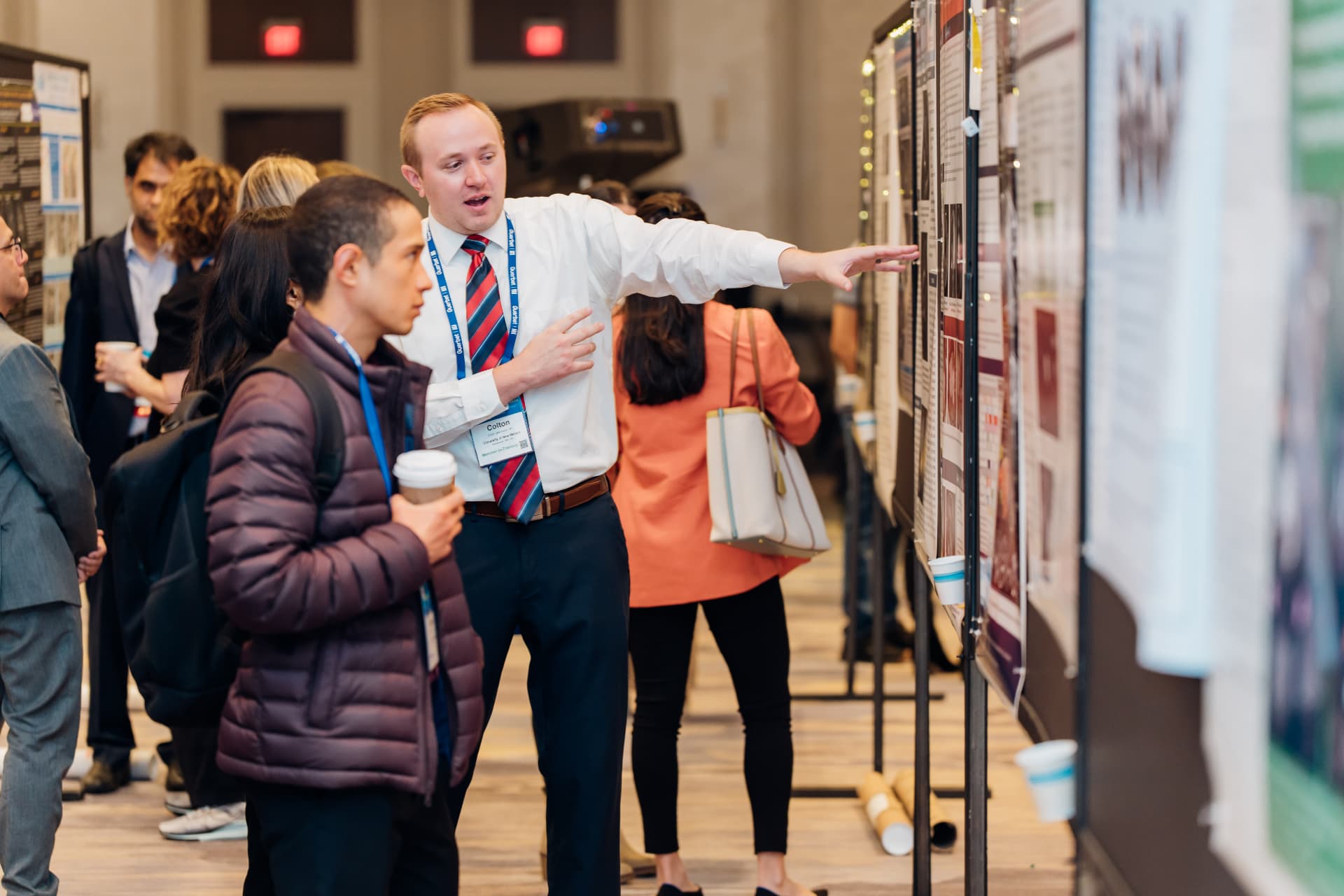 Corporate event photography of a presenter pointing to a research poster while attendees listen