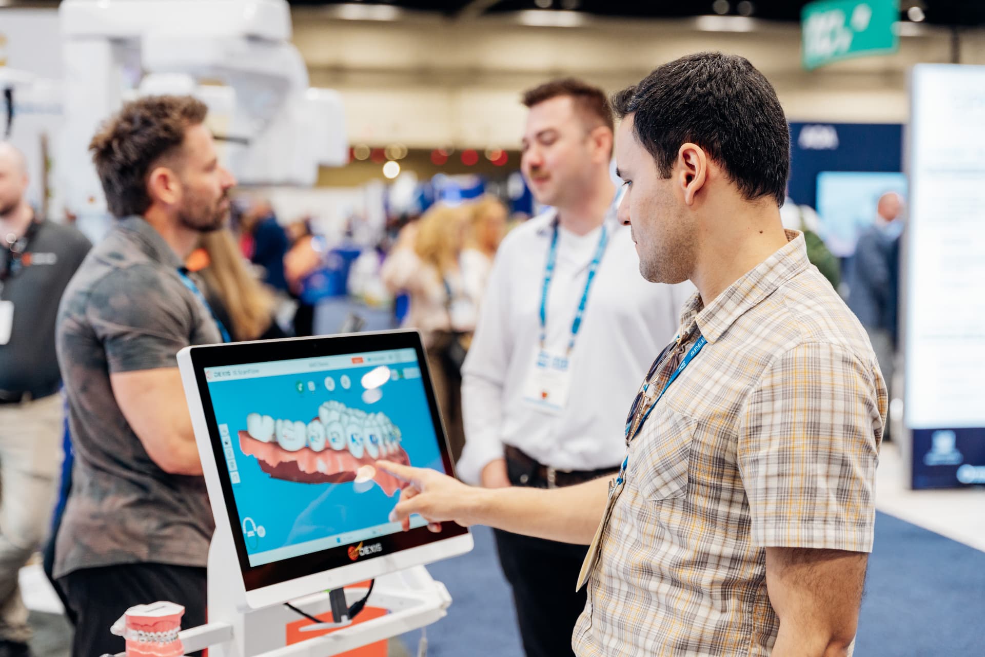 Corporate trade show photography of an attendee interacting with a 3D dental scanning touchscreen at an exhibitor booth