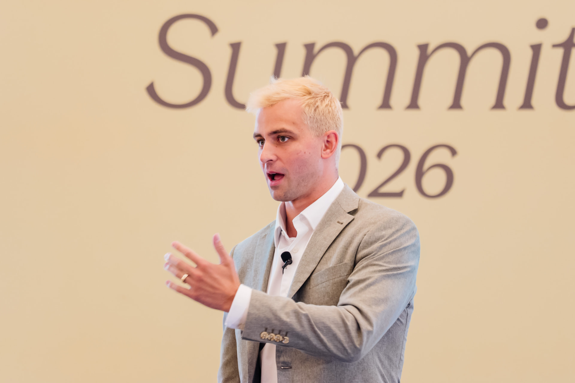 Corporate event photography of a speaker presenting in front of a large Summit 2026 stage screen