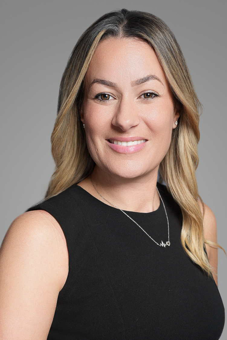Professional corporate headshot of a businesswoman on a gray studio backdrop, demonstrating polished executive portrait lighting